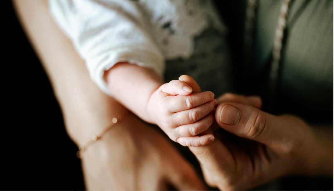 A parent's hand gently holding a newborn's hand